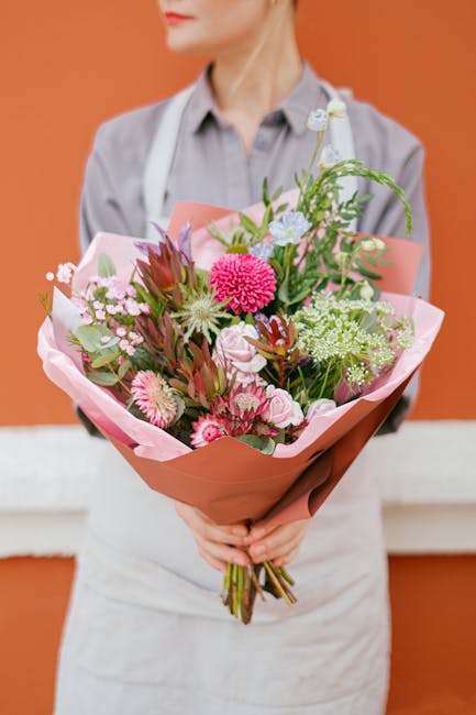 A person dressed in a light grey shirt and white apron holds a vibrant bouquet of fresh flowers from flowersUptonPark.co.uk, arranged as a floral gift ready for same day flower delivery near Upton Par